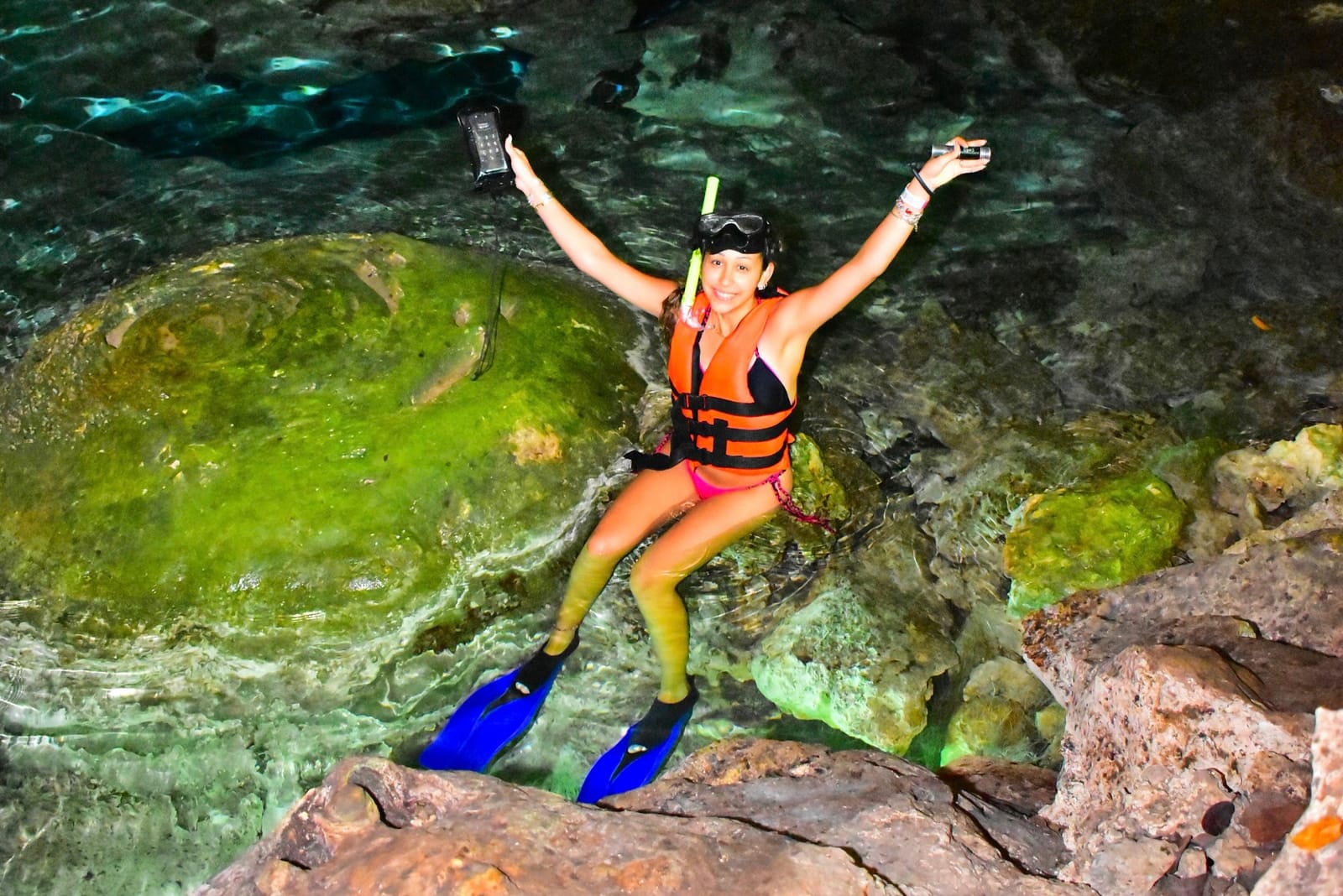 Guest in fins and life jacket celebrating on a cenote rock, underwater lamp in hand