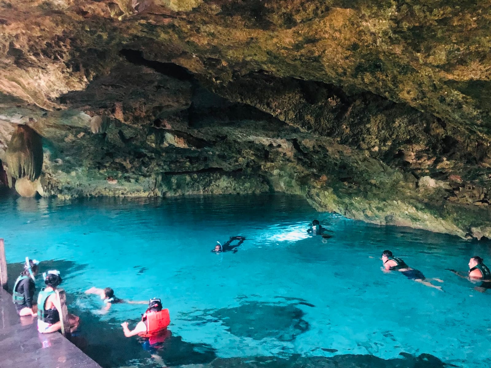 Group snorkelling in the turquoise water of Cenote Dos Ojos under the cavern ceiling