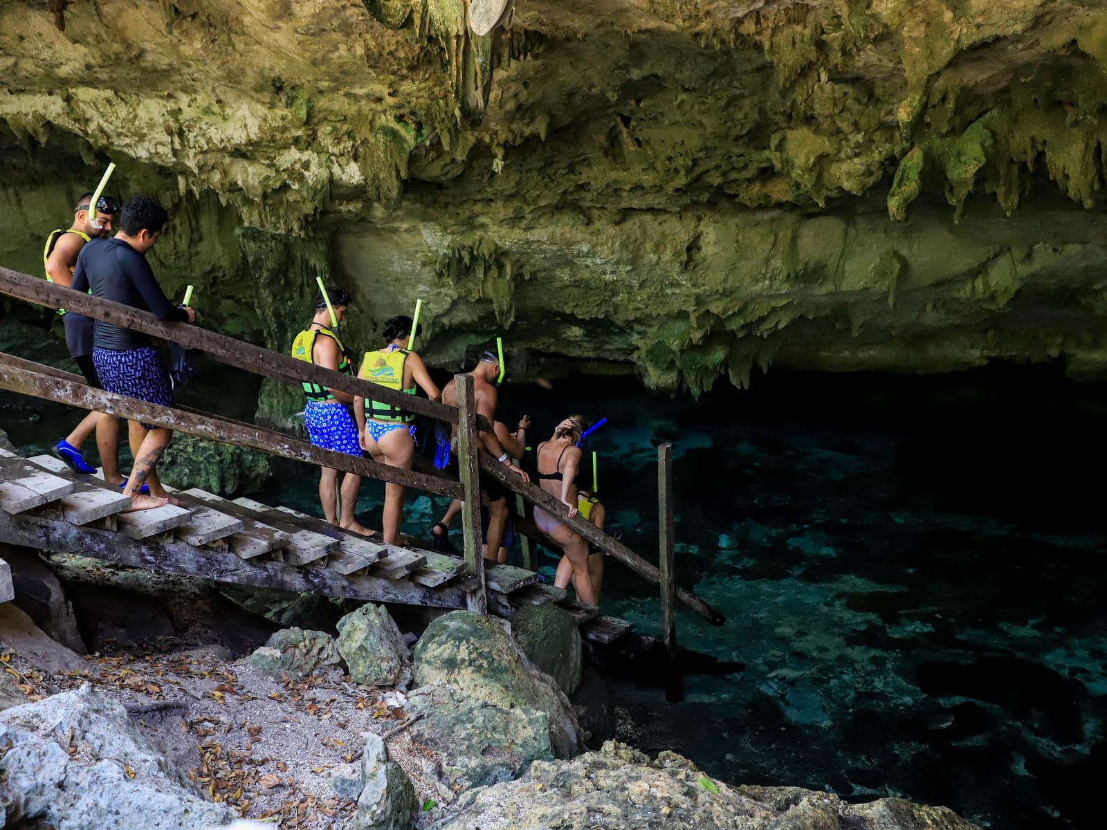 Small group walking down the wooden stairs into the water at Cenote Dos Ojos