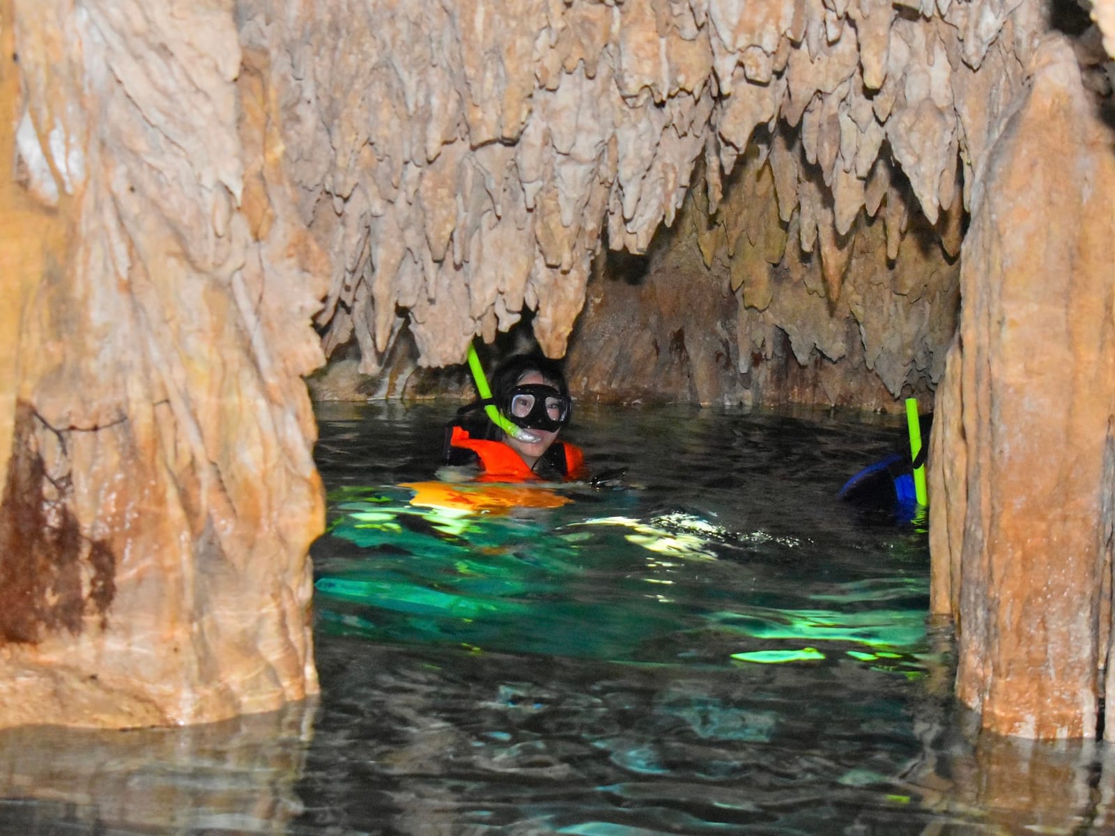 Snorkeller with mask and life jacket in a narrow passage between stalactites in the Dos Ojos caverns