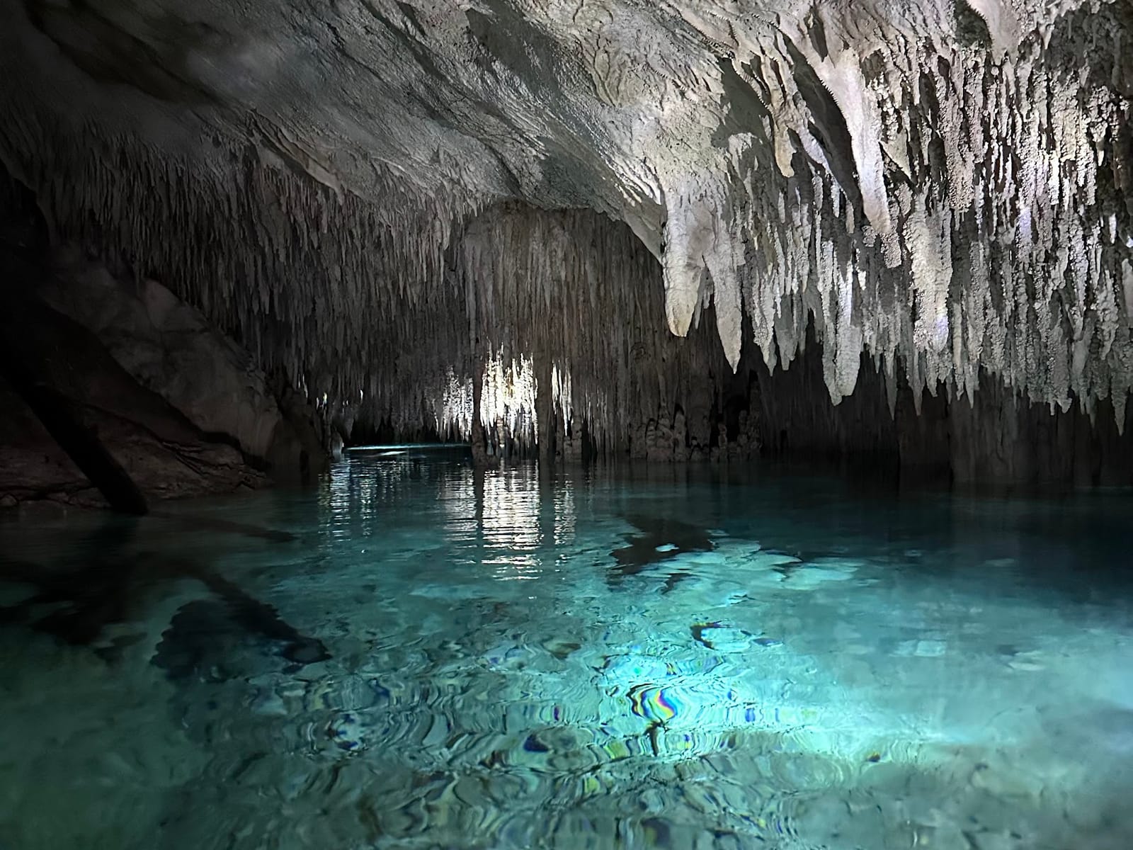 Gallery of white stalactites reflected in turquoise water in a passage of Cenote Los Monos