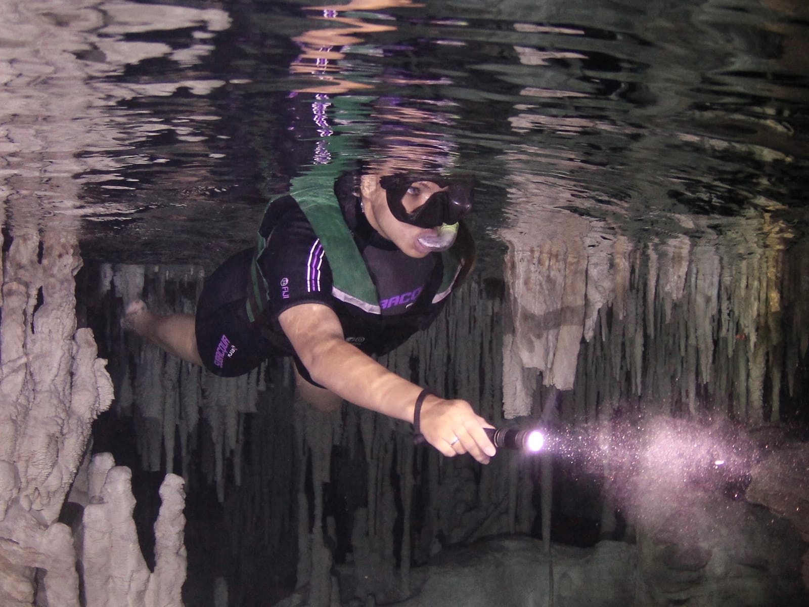 Snorkeler in a life vest lights up submerged stalactites with a dive lamp, Cenote Los Monos