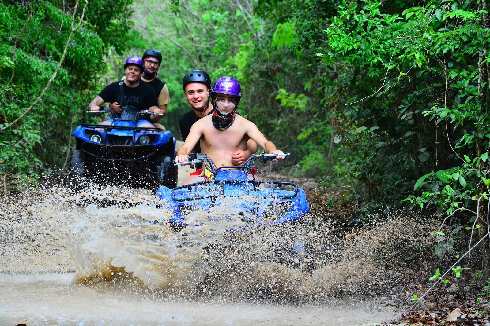 ATVs splashing through mud on a jungle trail near Akumal, riders in helmets