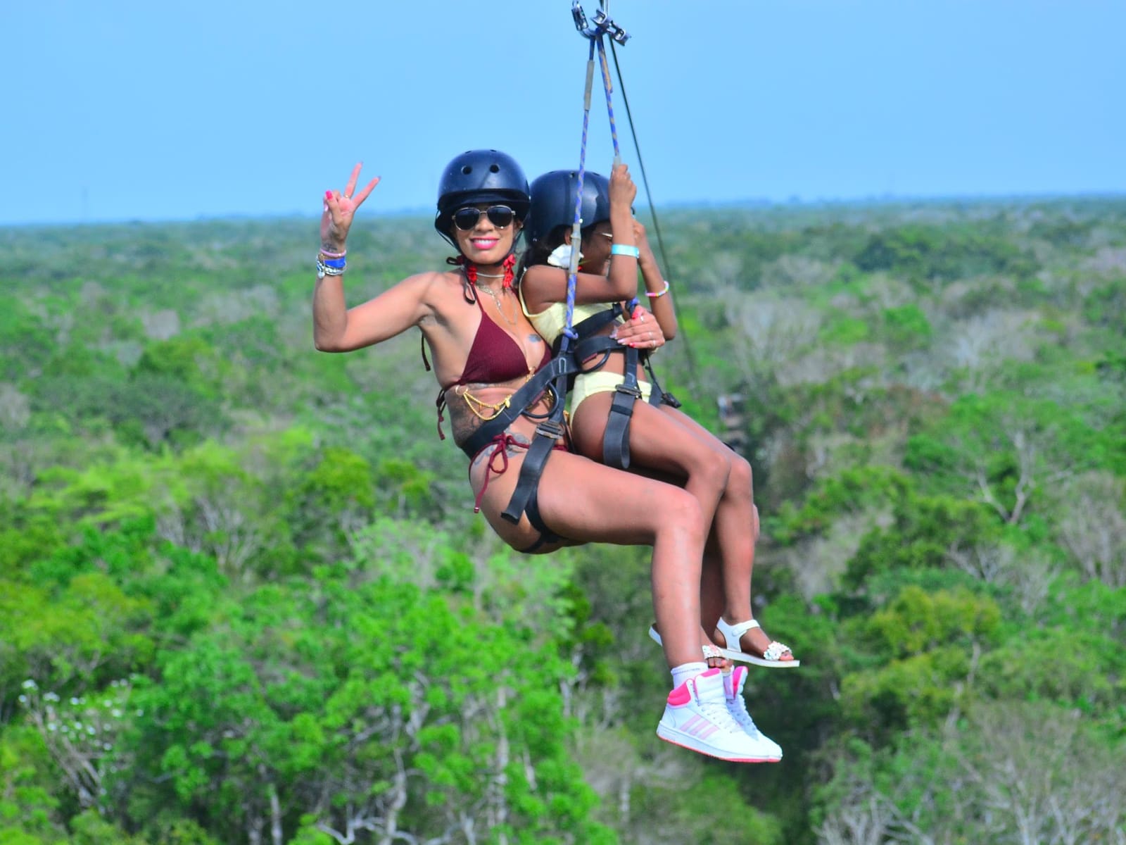 Adult and girl on a tandem zipline with helmets and harnesses above the jungle