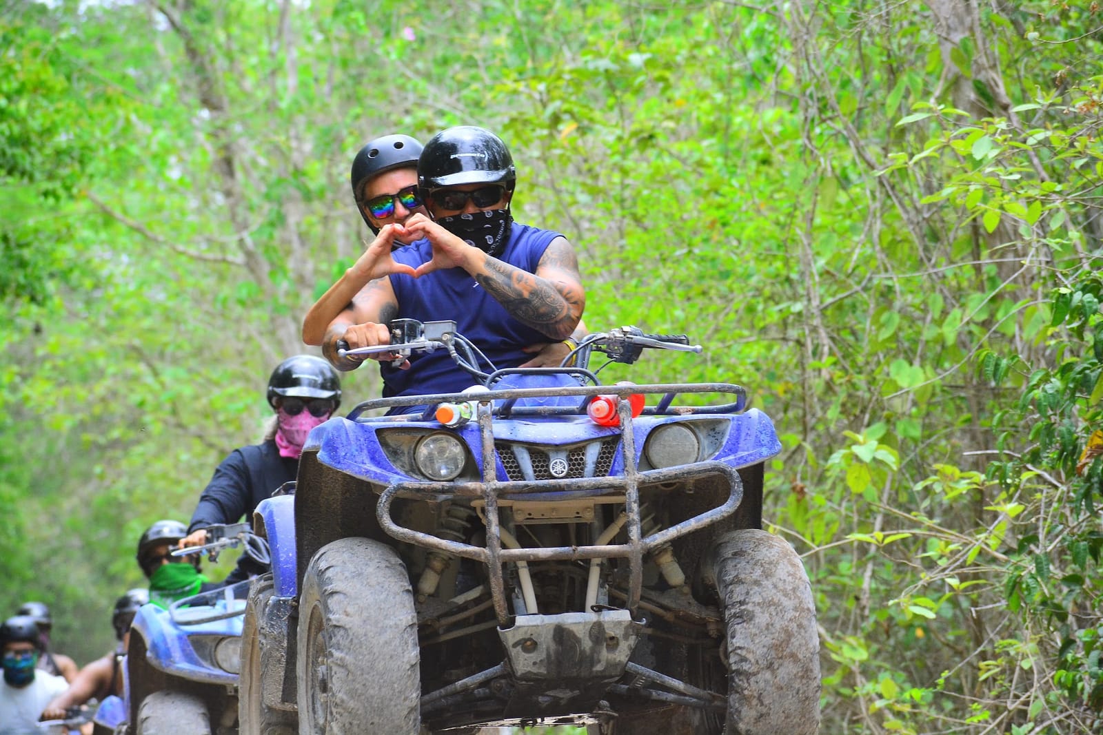 Couple in helmets making a heart with their hands on an ATV in the jungle