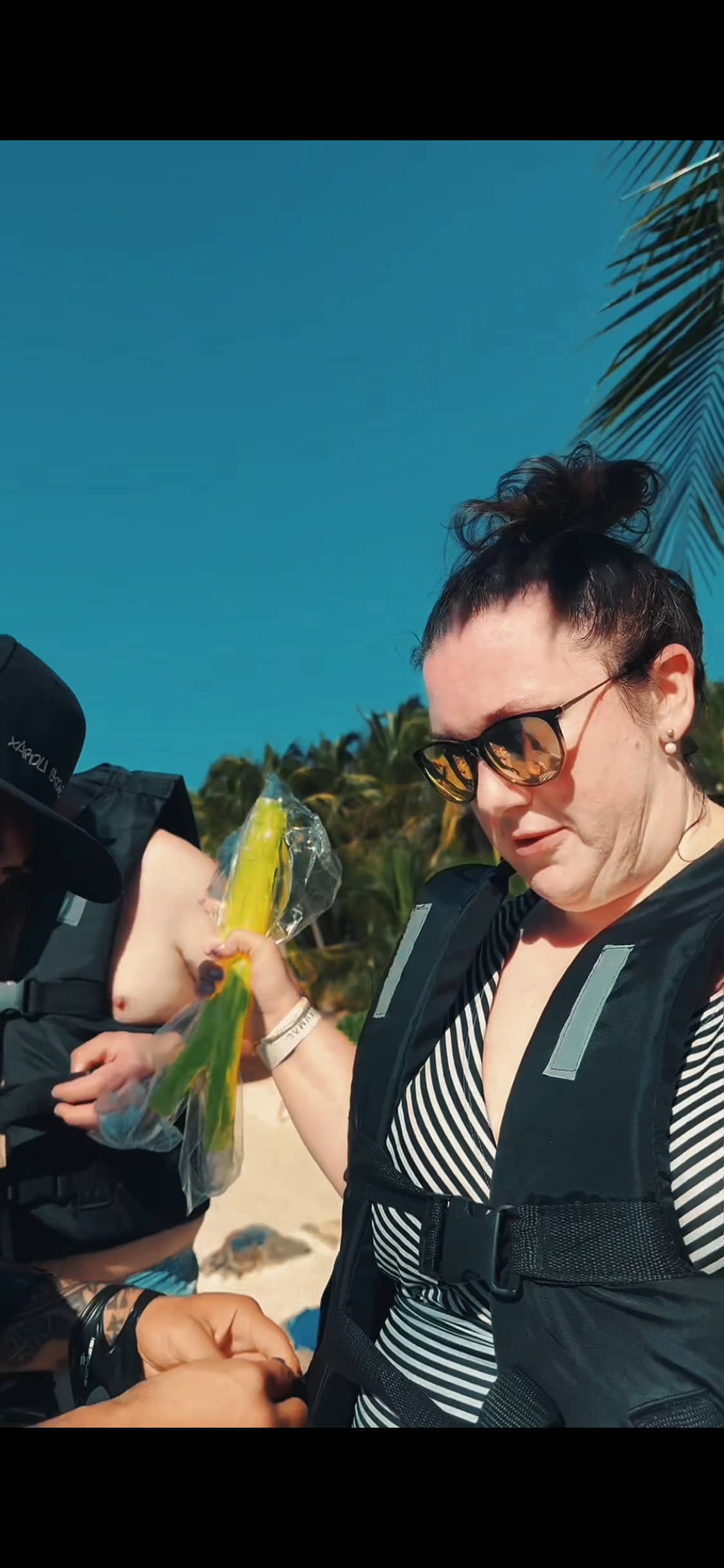 Guest in life vest holds a fishing lure on Akumal Bay beach, ready for sport fishing with Akbay Tours