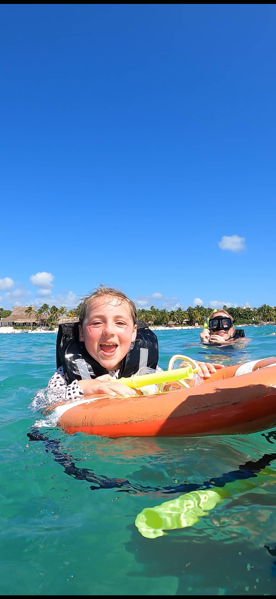 Happy child with life jacket and snorkel gear floating in turquoise water at Akumal Bay