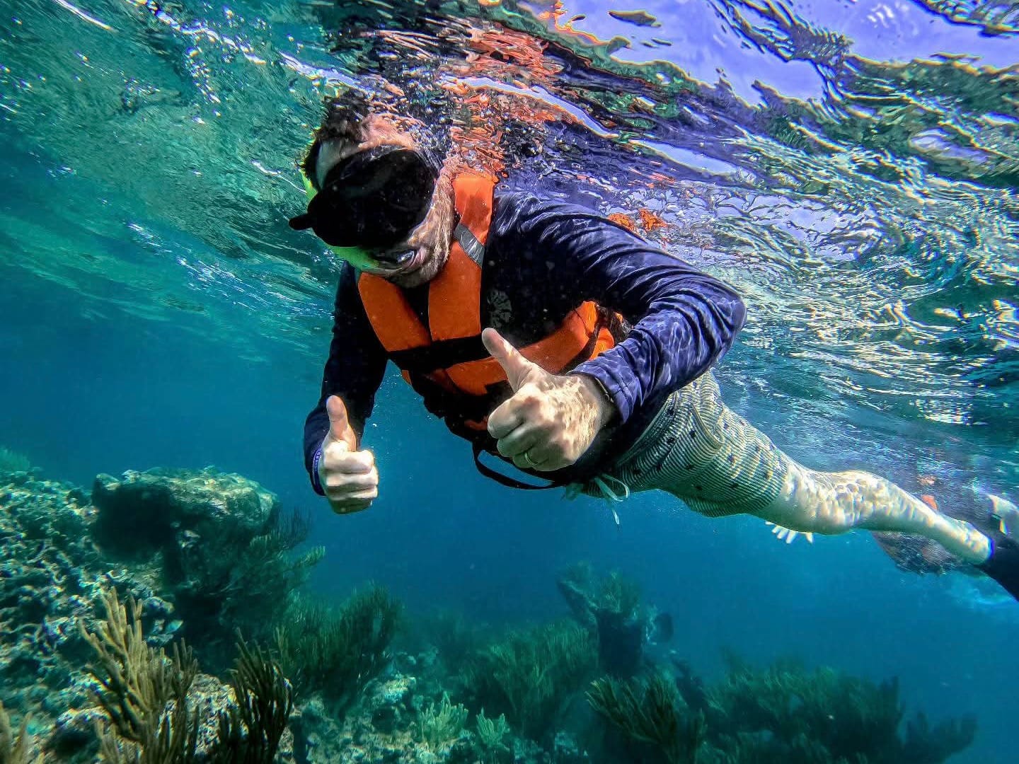 Snorkeler in a life jacket and UV shirt giving two thumbs up over the reef