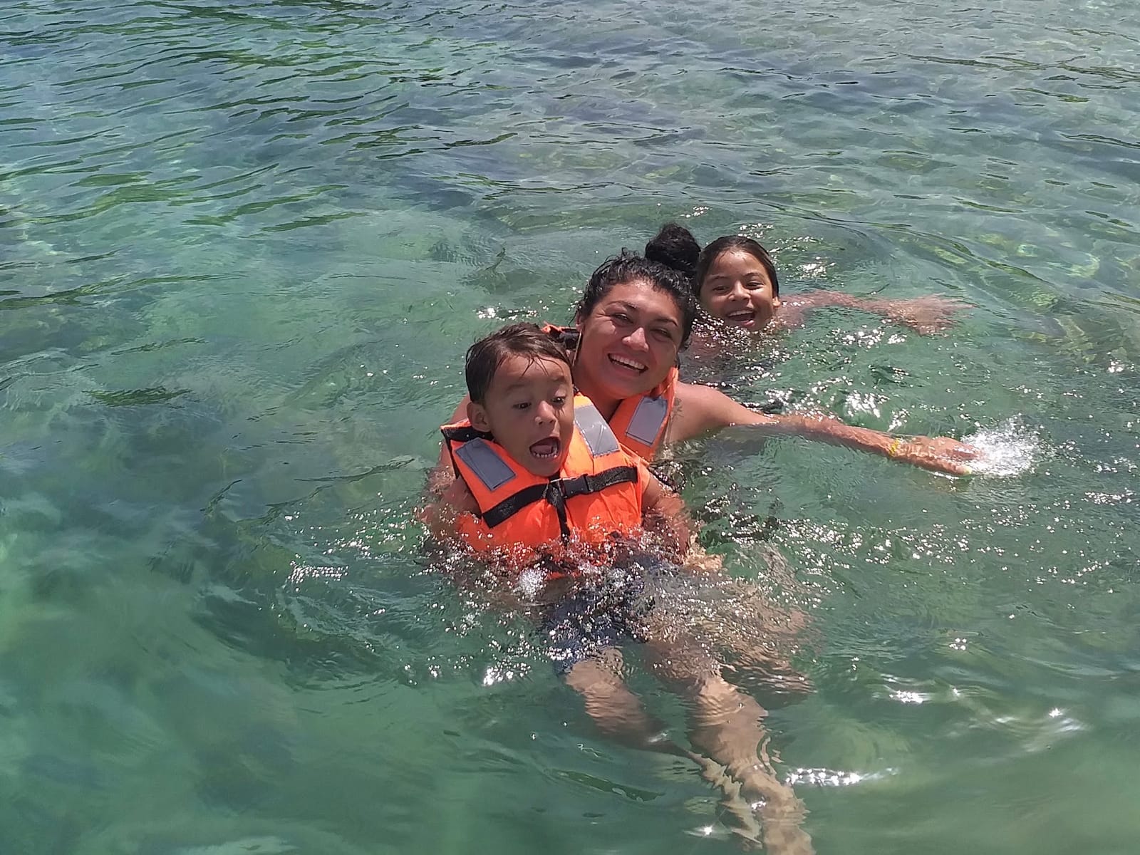 Mother and kids in life jackets laughing as they swim in the clear green lagoon water