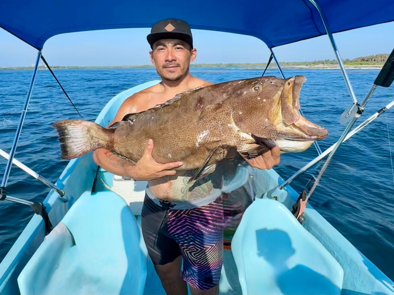 Angler holding a large grouper under the boat's canopy