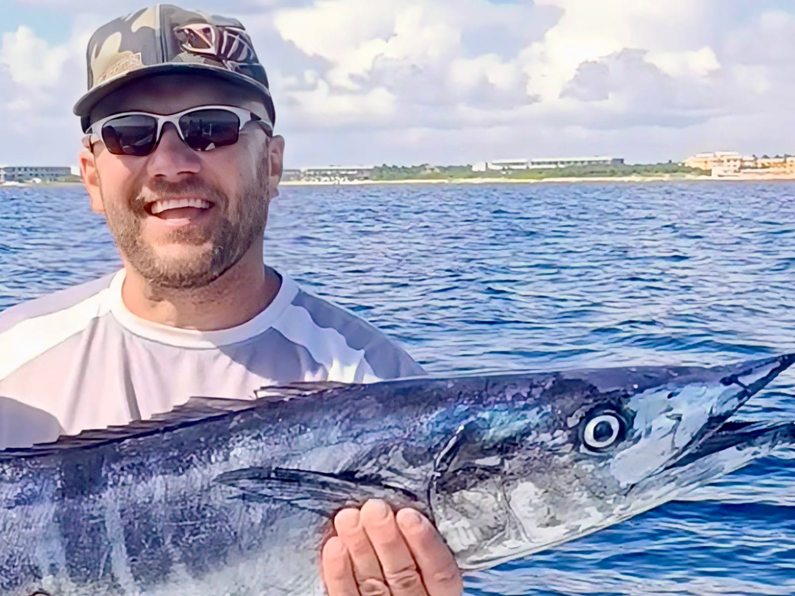 Smiling angler with a wahoo on board, coastline in the background