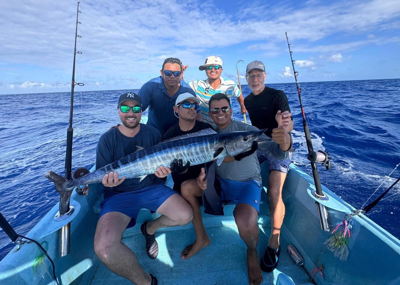 Small group and crew with a wahoo on the boat, open sea behind
