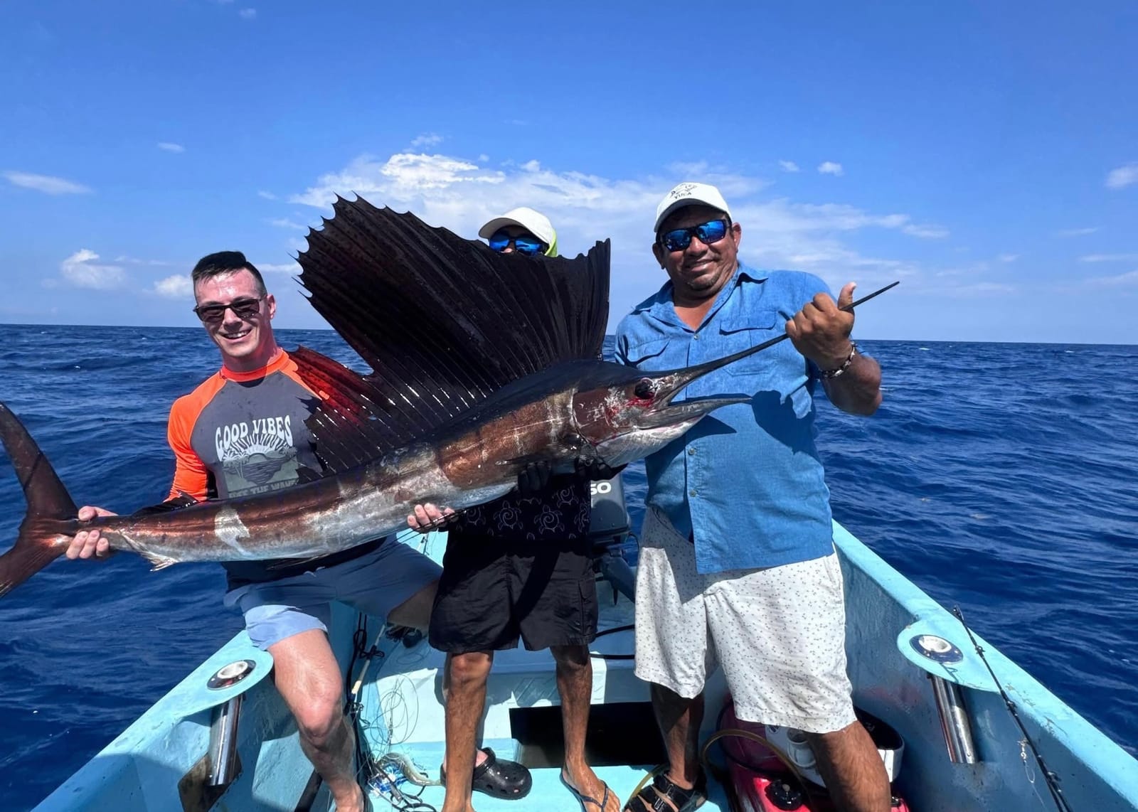 Guest and crew holding up a sailfish caught aboard the private fishing boat, open sea behind
