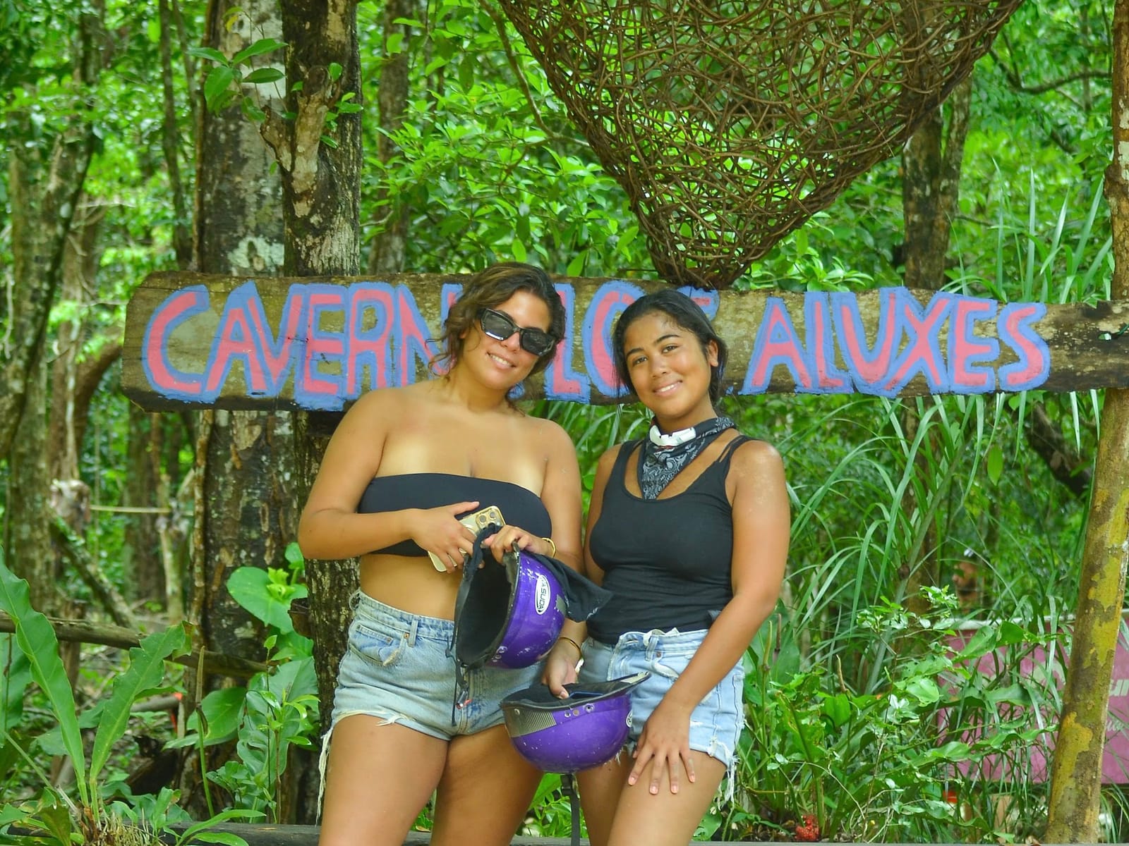 Two guests with their helmets by the Caverna de los Aluxes sign