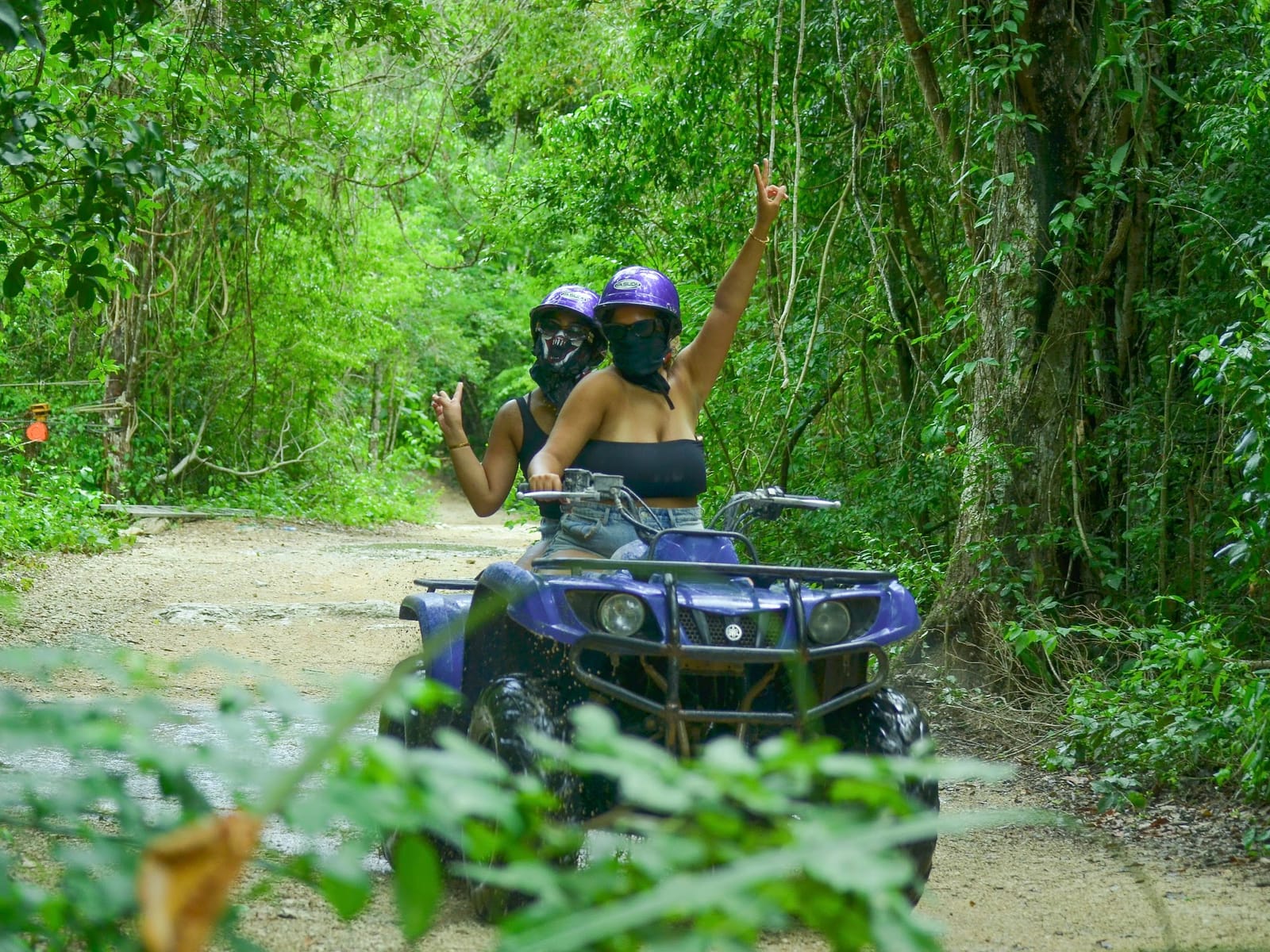 Two riders in helmets on a double ATV on a jungle trail near Akumal